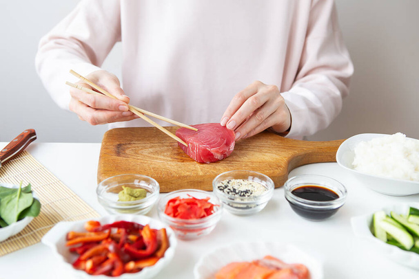 Het bereidingsproces van sushi, het bereiden van alle ingrediënten voor sushi, het meisje houdt tonijn vast met stokjes - Foto, afbeelding