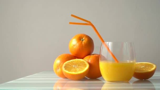 Succo d'arancia in un bicchiere circondato da arance naturali con sfondo bianco chiaro naturale - Filmati, video