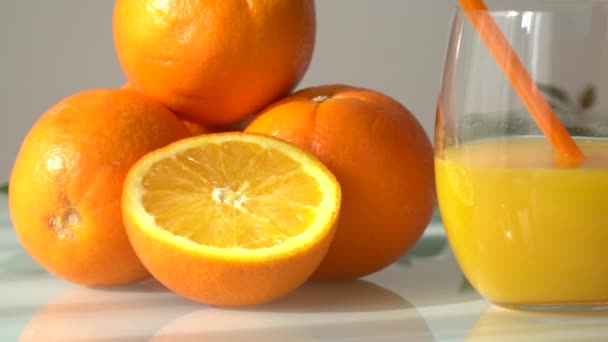 Orangensaft in einem Glas, umgeben von natürlichen Orangen mit einem natürlichen Sonnenlicht weißen Hintergrund - Filmmaterial, Video