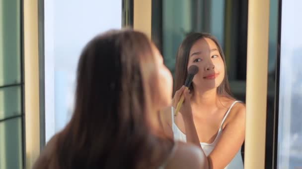 Portret piękna młoda azjatycka kobieta stosowania kosmetyków przez lustro wnętrza łazienki - Materiał filmowy, wideo