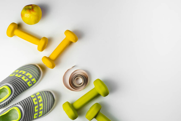 Gym and workout, sports shoes, sneakers, Healthy lifestyle concept foto. Flat lay of sport. Athlete's set with centimeter tape, green apple and dumbbells on a grey background - Photo, Image