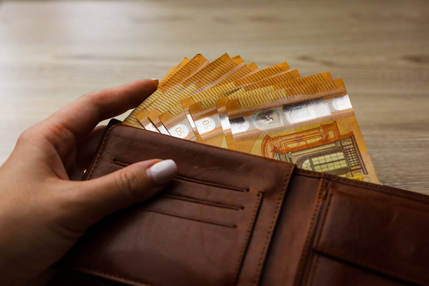 Op de houten tafel gepropt eurobankbiljet in portemonnee. Gevulde leren portemonnee. Euro-facturen in portemonnee. - Foto, afbeelding