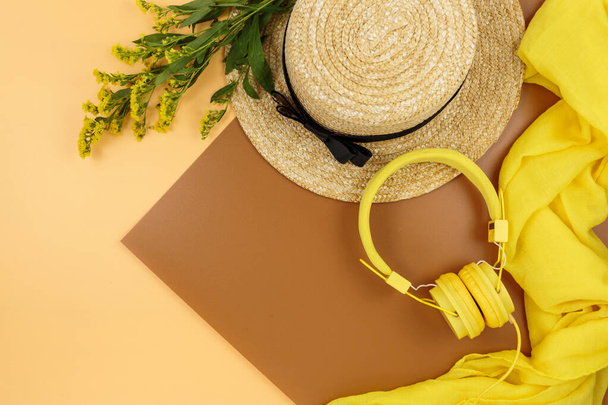 麦わら帽子、茶色の背景にフィールドイエローの花。流行のファッションアクセサリー。フラットレイアウト、閉じます。夏休み休日のコンセプト. - 写真・画像