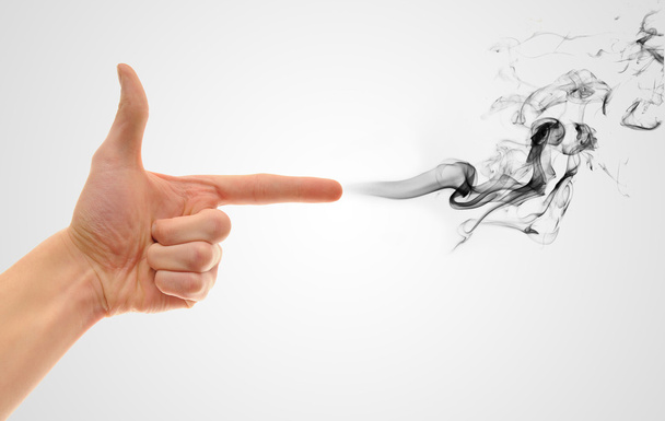 A hand making a shape of a pointed hand gun on white gradient background with black smoke coming out of the finger - Foto, Imagen