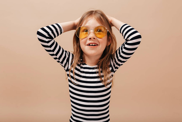Close up portrait of adorable pretty girl in round trendy glasses and stripped dress holding up hands and smiling. High quality photo - Photo, Image
