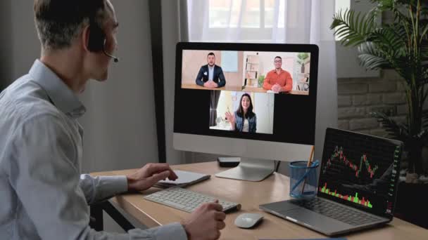 オンライン会議ビデオ通話。成功した大人のビジネスマンは、職場に座っている間にコンピュータを使用してビデオ通話で多人種間のビジネス同僚と会話をし、対話者を迎える - 映像、動画