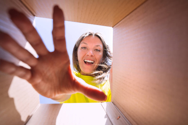 Onnellinen tyytyväinen nainen unboxing toimitus paketti. Näkymä laatikosta. Onnellinen nainen vie tavarat pahvilaatikosta tai pakettipaketista verkkokaupasta. Nainen purkulaatikon kanssa - Valokuva, kuva