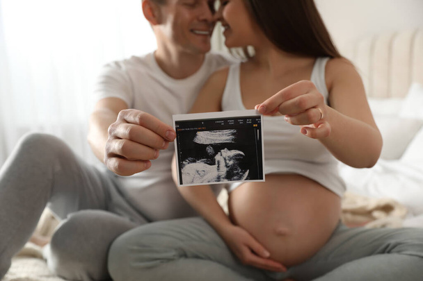 Young pregnant woman with her husband in bedroom, focus on ultrasound picture of baby - Фото, зображення