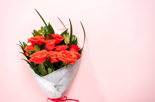 Pose plate. Bouquet de roses rouges et de feuilles vertes sur fond rose. - Photo, image