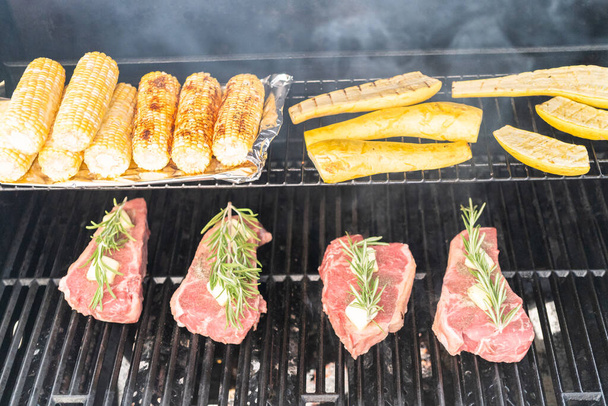 Grilling New York steak with a slice of butter and rosemary on an outdoor gas grill. - Photo, Image