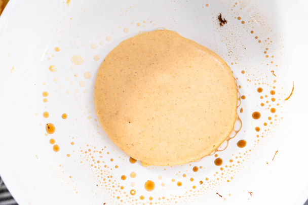 Frying pumpkin pancakes batter on a white frying pan. - Фото, изображение