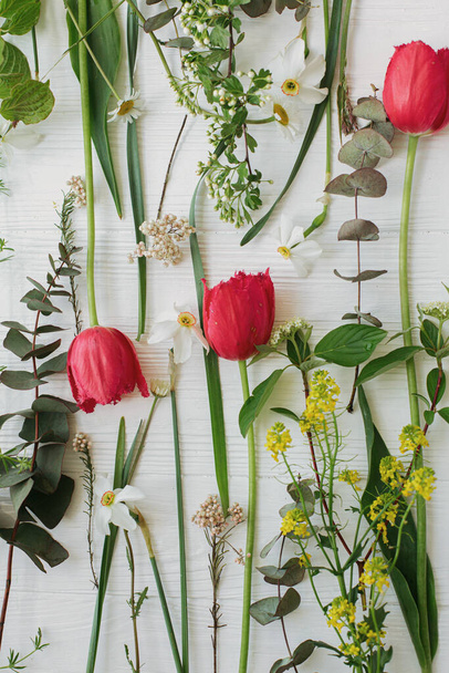 Piękne czerwone tulipany, żonkile, eukaliptusowy układ kwiatów na rustykalnym białym drewnianym tle, płaskie leżały. Szczęśliwego Dnia Matki. Szczęśliwego Dnia Kobiet. Witaj wiosenna kartka z życzeniami - Zdjęcie, obraz