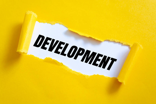 Rozerwany żółty papier na białej powierzchni ze słowami Development. - Zdjęcie, obraz