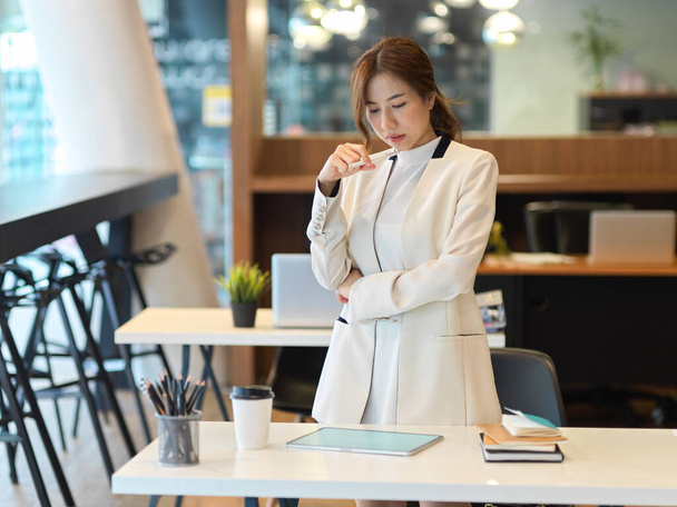 Portrét mladé krásné ženy ve společenském obleku stojící a dívající se na digitální tablet na kancelářském stole - Fotografie, Obrázek