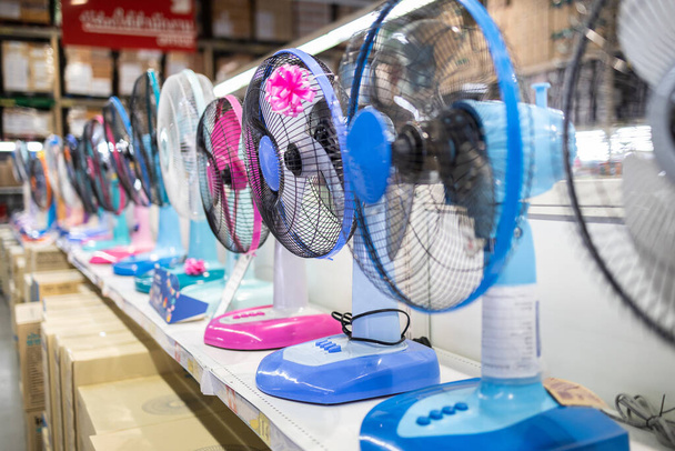 Ventilador para enfriar en una tienda de electrónica, varias marcas de ventiladores eléctricos se exhiben en un estante en el supermercado en un día soleado y caluroso de verano, eligiendo comprar electrodomésticos energéticamente eficientes, ahorrar concepto de energía - Foto, Imagen
