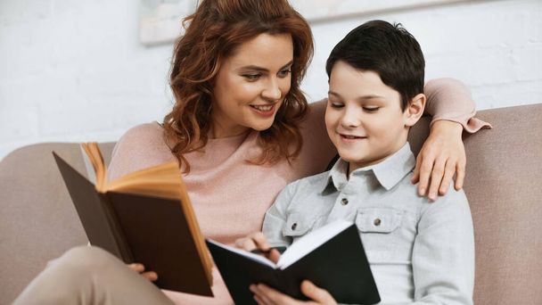 Smiling mother holding book near son with notebook during education at home  - Foto, Imagen