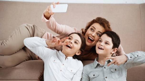 Cheerful family showing peace sign while taking selfie on couch  - Valokuva, kuva