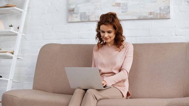 Woman using laptop while working on couch at home  - Foto, Bild