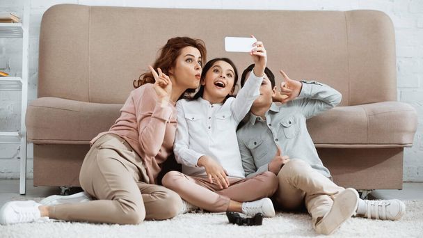 KYIV, UKRAINE -  APRIL 15, 2019: Family taking selfie on smartphone near joystick on floor at home  - Photo, image
