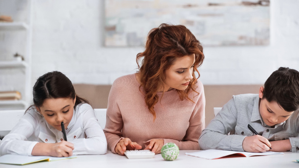 Mother helping kids with homework near calculator on table  - Photo, Image