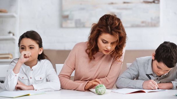 Woman using calculator near pensive daughter and son writing on notebook at home  - Photo, Image
