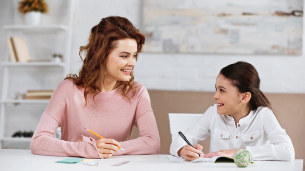 Cheerful mother and kid doing homework at table  - Photo, Image