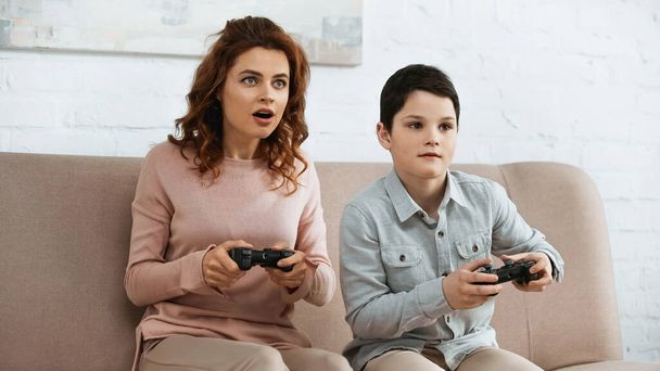 KYIV, UKRAINE -  APRIL 15, 2019: Excited mother playing video game with son on couch  - Foto, immagini