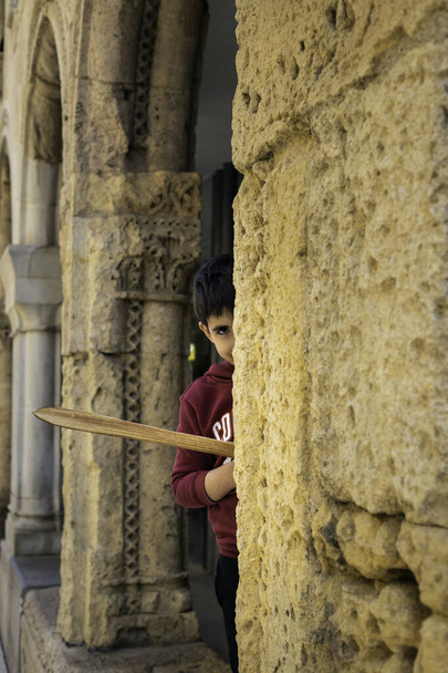 Chłopiec z drewnianym mieczem wygląda ciekawie za kamienną kolumną Koncepcja stylu życia - Zdjęcie, obraz