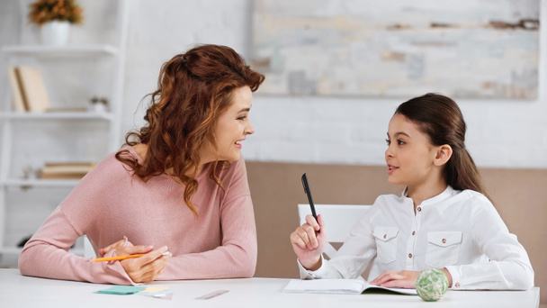 Sorridente madre sostenere figlia con i compiti a tavola  - Foto, immagini