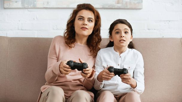 KYIV, UKRAINE -  APRIL 15, 2019: Focused mother and daughter playing video game at home  - Foto, Imagen