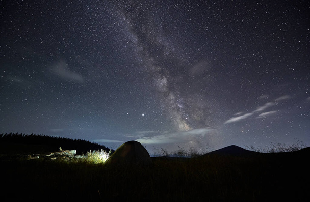 Amazing starry night sky in the mountains and tent at campsite. Millions of stars over single tent in the middle of mountain meadow. Concept of closeness with nature and astrophotography - Foto, imagen
