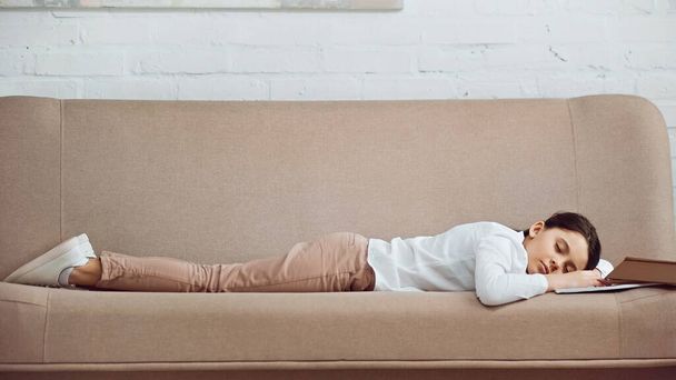 Chica preadolescente durmiendo cerca de libro en el sofá en casa  - Foto, Imagen