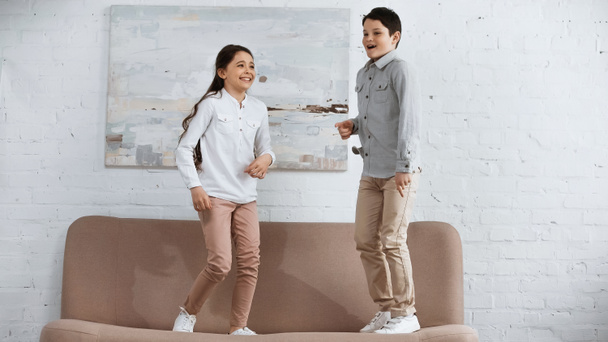 Cheerful kids standing on couch in living room  - Foto, afbeelding
