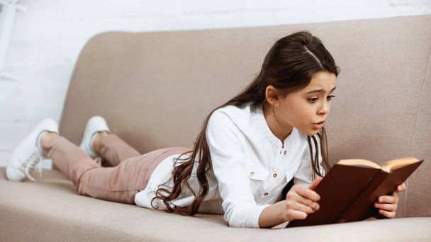Preteen girl reading book on blurred foreground at home  - Foto, Imagem
