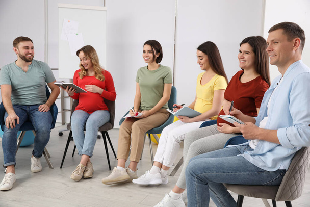 Группа беременных женщин с мужчинами и врачом на курсах для будущих родителей в помещении - Фото, изображение