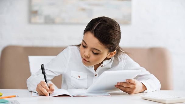 Nastolatka pisząca na notatniku i korzystająca z tabletu cyfrowego podczas edukacji online  - Zdjęcie, obraz