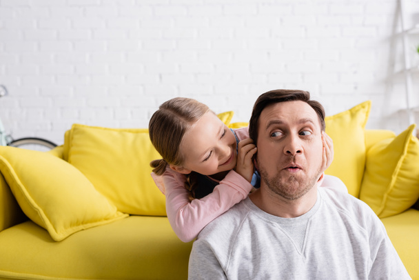 joyful girl plugging ears of grimacing father while having fun at home - Photo, Image