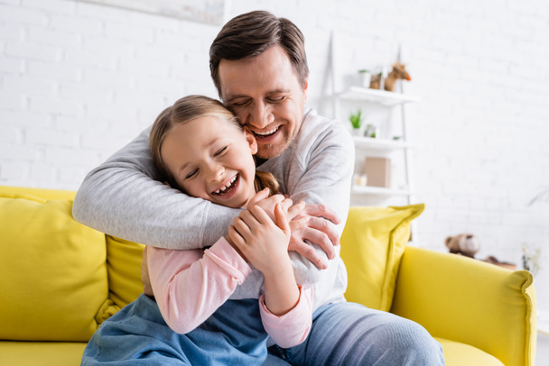 laughing man hugging daughter on couch in living room - Fotoğraf, Görsel