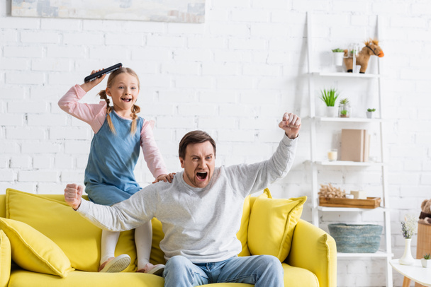 excited man shouting and showing win gesture while watching tv with daughter - Φωτογραφία, εικόνα