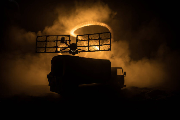 Creative artwork decoration. Silhouette of mobile air defence truck with radar antenna at night. Rocket launcher aimed at sky ready to attack. Selective focus - Photo, Image