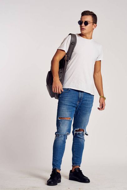 ein Mann mit Rucksack auf dem Rücken in Jeans-T-Shirt, Turnschuhen und Brille im Gesicht - Foto, Bild