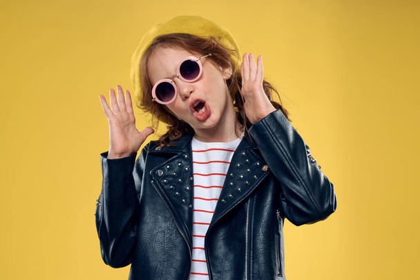 Весела маленька дівчинка в сонцезахисних окулярах та капелюсі студія жовтого фону моди
 - Фото, зображення