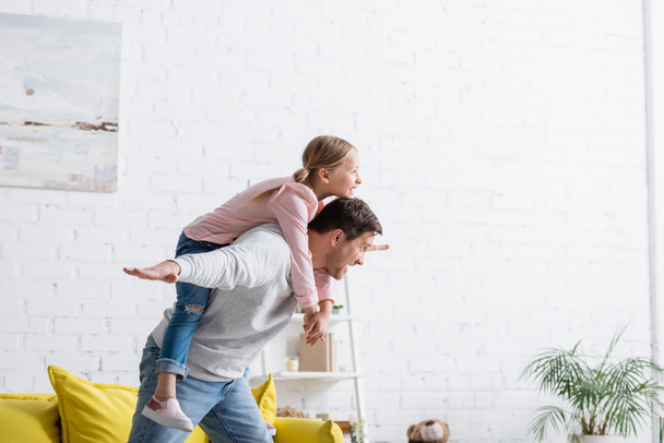 excited father piggybacking cheerful daughter at home - Foto, afbeelding