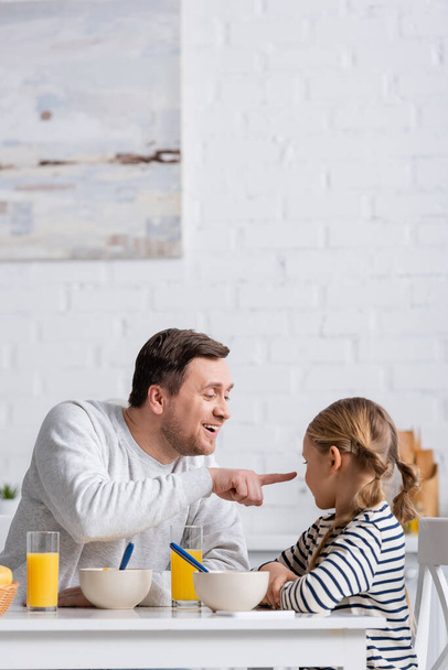 cheerful father pointing at daughter while having fun during breakfast - Foto, Imagem