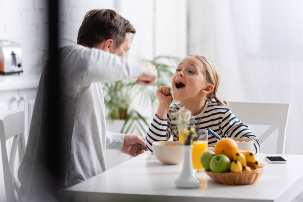 girl with open mouth near father feeding her with breakfast on blurred foreground - Photo, Image