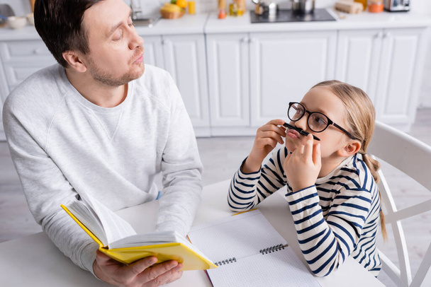 игривая девушка держит ручку возле носа, делая домашнее задание с отцом - Фото, изображение