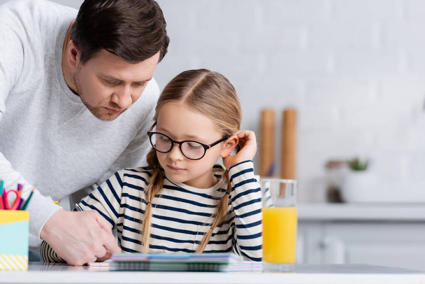 father helping daughter doing homework in kitchen, blurred foreground - Фото, изображение