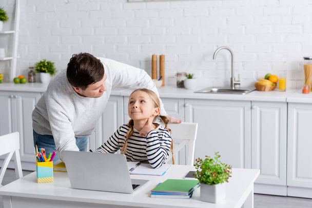 father and daughter looking at each other during online lesson in kitchen - Fotoğraf, Görsel
