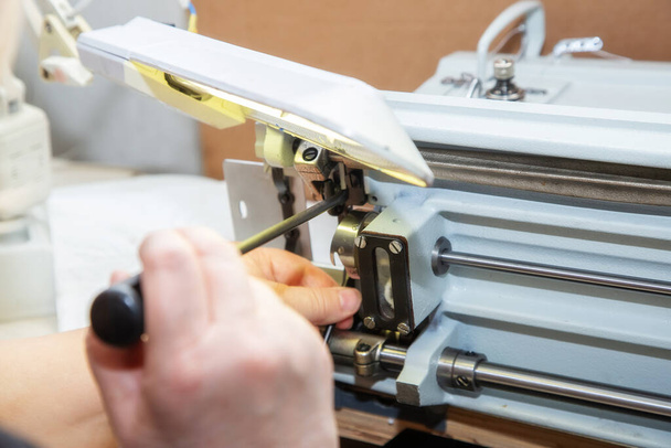 Tornavidayla kadın elleri dikiş makinesinin mekiğini tamir ediyor. Evdeki endüstriyel dikiş makinesinin tamiri. Bakım. - Fotoğraf, Görsel