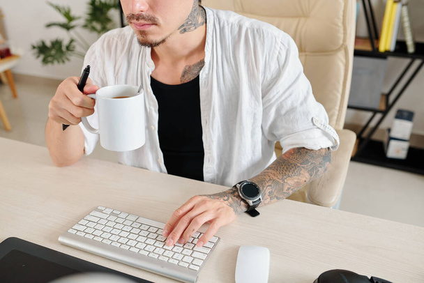 Imagen recortada del diseñador gráfico con tableta digital bebiendo café de la mañana y revisando correos electrónicos en la computadora - Foto, Imagen